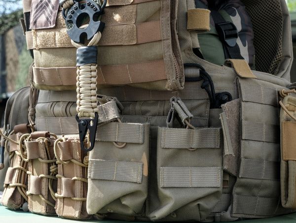 Close-up of tactical vest with multiple pouches and attachments outdoors.