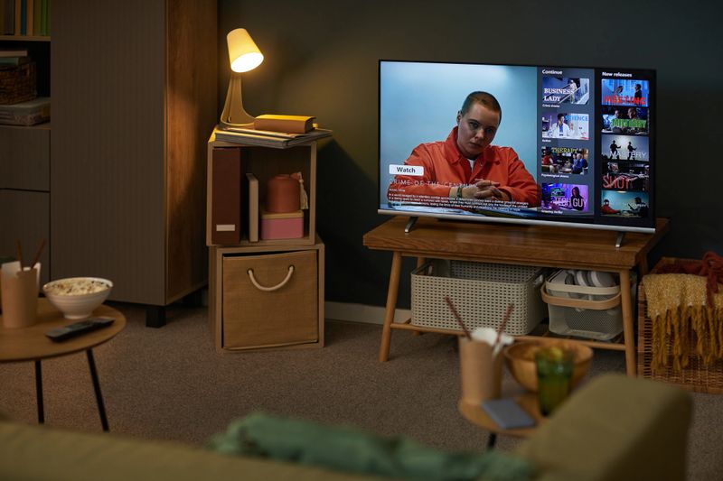 Living room scene showing modern television displaying streaming service interface with female character on screen, popcorn bowl and drinks on table, cozy home entertainment setup