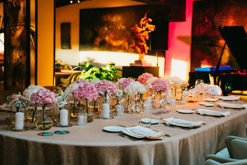 Luxurious table set for an elegant gathering featuring pink and white floral centerpieces, candles, and polished dinnerware in a sophisticated environment designed for a special event.