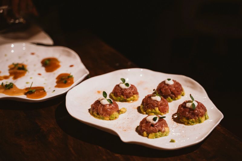 Exquisite arrangement of tuna tartare served atop a bed of avocado, beautifully garnished on an artistically shaped plate, highlighting sophisticated culinary presentation