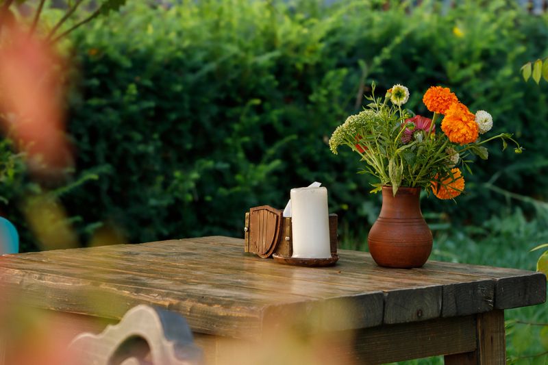 still life vintage patio pattern in garden rustic aesthetic cottage core concept wooden table with candle and flower vase in spring season blossom floral environment space colorful peaceful day time
