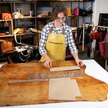 A woman in a yellow apron working with leather and patterns in a workshop.