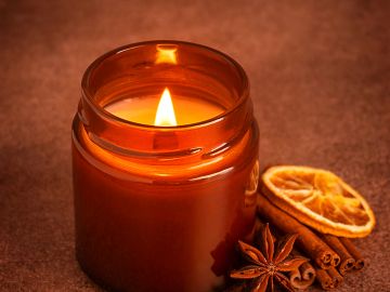 Lit candle in a brown jar with dried orange and spices.