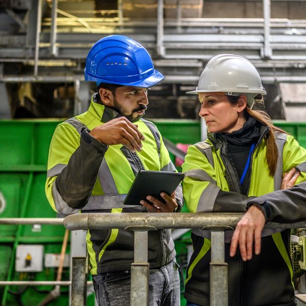 Male and female engineers in PPE discussing work in a warehouse environment