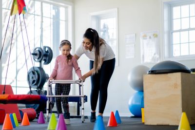Therapist assisting a young girl with a walker through an obstacle course.