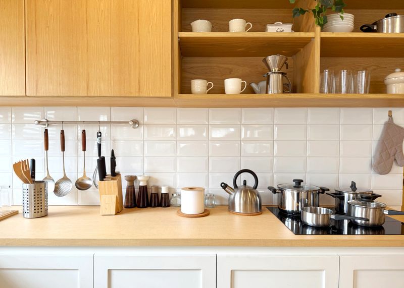 Clean and organized modern kitchen interior with wooden cabinets, white tiled backsplash, and stainless steel appliances. Minimalist Scandinavian style, cozy home cooking space. Bright and inviting.