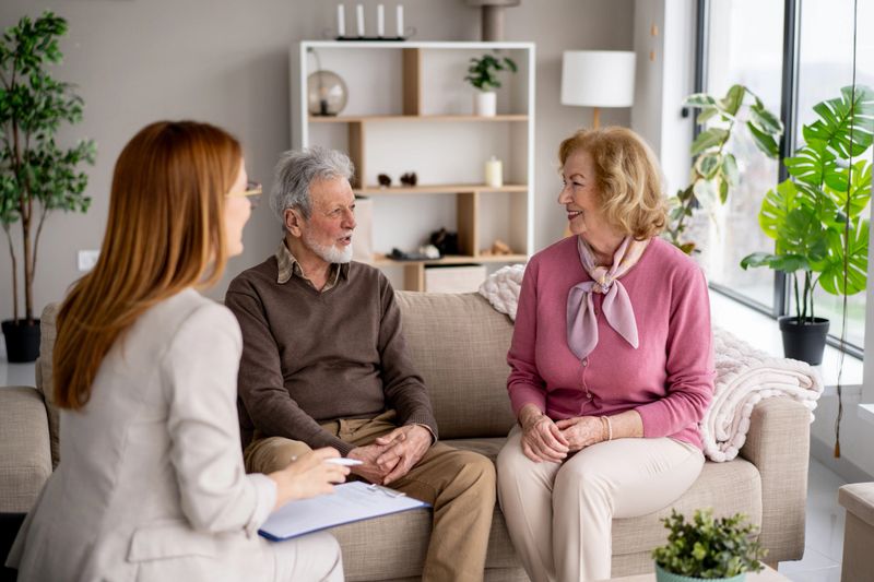 An elderly couple enjoys a lively conversation with a consultant in their well-decorated living room, radiating positivity and connection.