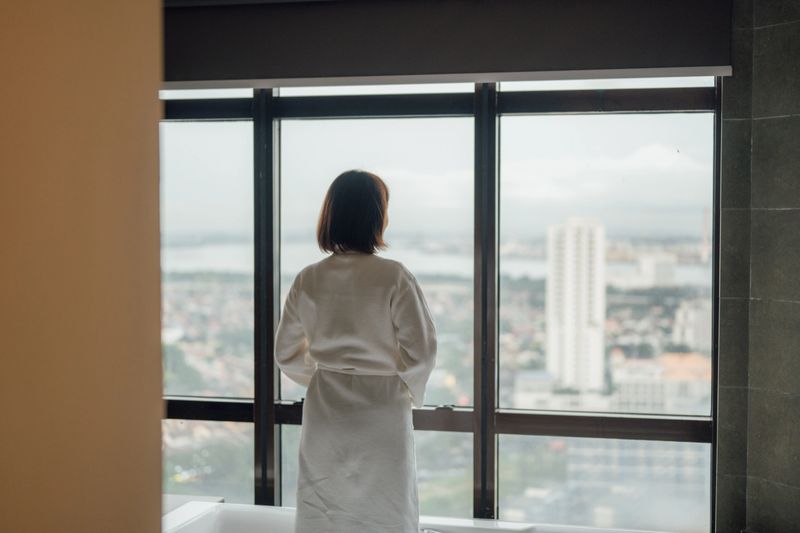 A beautiful Asian woman poses in a bathrobe before bathing, standing on the edge of a bathtub in a modern home bathroom. Concept: wellness and beauty routine.