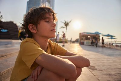 Boy sitting with eyes closed at sunset outdoors.