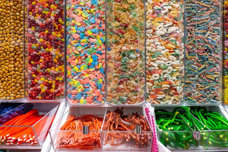 Colorful gummies, candies, marshmallows, and sweets in transparent shop containers, assorted confectionery products displayed for sale.
