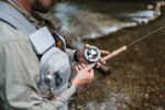 Man fly fishing in a river, focusing on his reel.