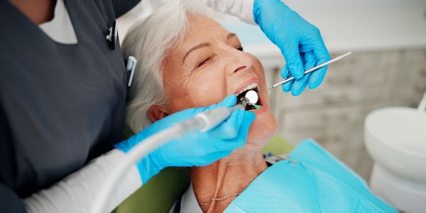 Dentist cleaning patient's teeth with a prophy angle and polishing cup holding a mouth mirror and we