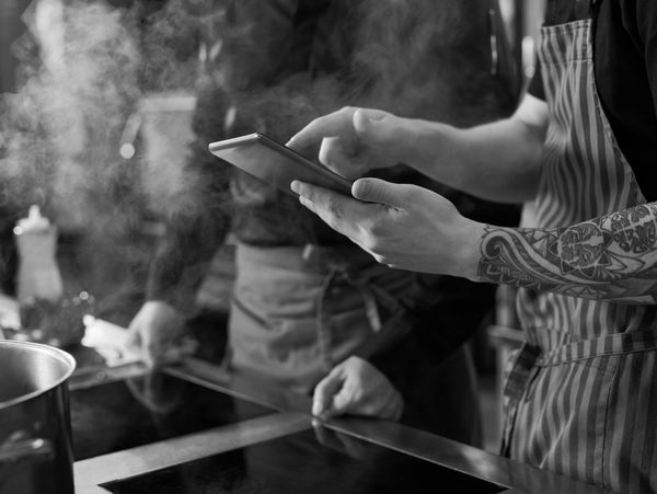 Chef with tattoos using a tablet in a steamy kitchen.