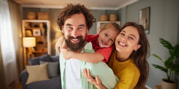 Happy family of three smiling together in a cozy living room.