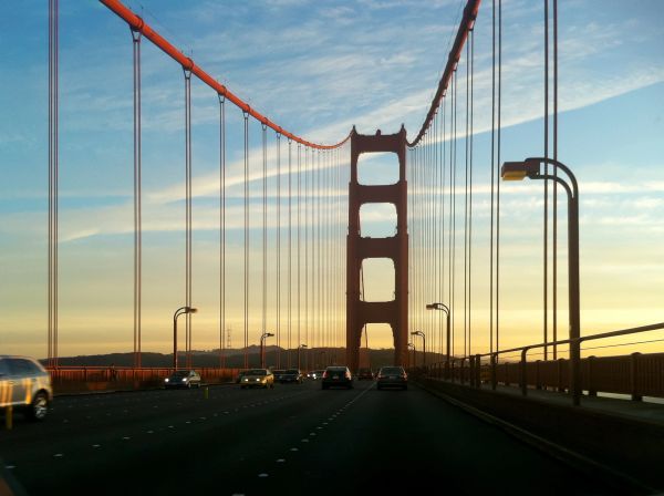 Golden Gate Bridge at sunset with cars crossing.