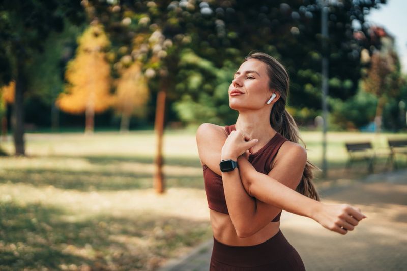 Young woman in sportswear checking her smartwatch after finishing yoga in the park, tracking fitness progress and monitoring activity levels. Concept of healthy lifestyle, wellness, and modern wearable technology.