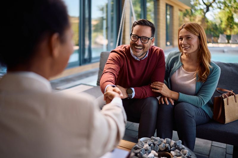 Happy couple coming to an agreement with their real estate agent. Focus is on man handshaking with the agent.