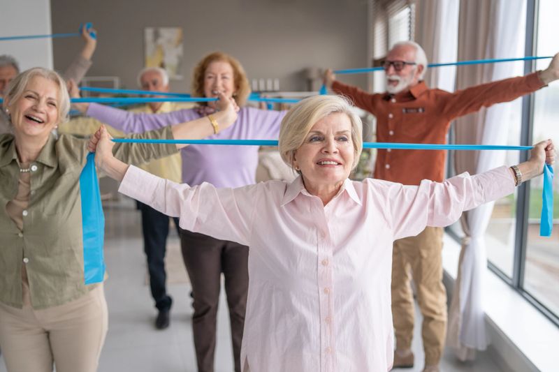 A group of seniors is participating in a fitness exercise class, using resistance bands to promote health and well-being in a supportive environment.