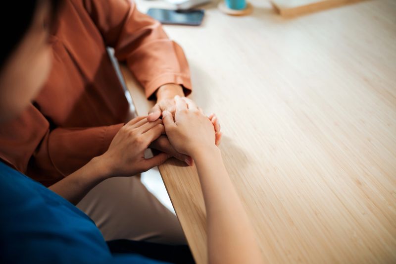 Close-up of caregiver holding hands with elderly woman