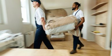 Two movers carrying a wrapped mattress.