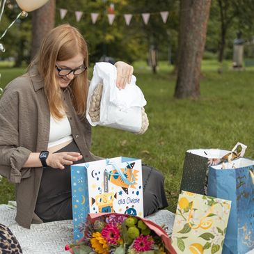 A woman unwrapping gifts outdoors on a picnic blanket.