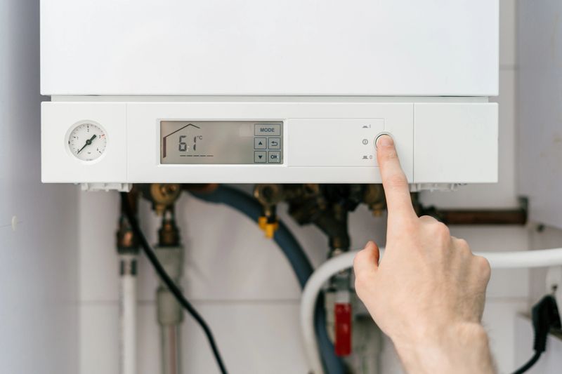 POV of a repairman is pressing a button on a gas boiler in a residential bathroom, choose temperature on the digital control panel to adjust system for efficient heating management.