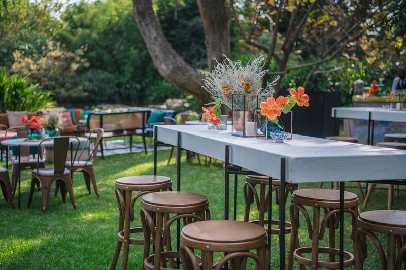 Vibrant and inviting outdoor setting showcasing elegantly arranged tables with wooden stools and floral decorations. Ideal for hosting events, including weddings, parties, and intimate gatherings, surrounded by lush greenery and natural ambiance.