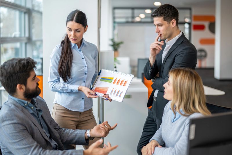 Businesswoman holding and presenting business results with charts while discussing them with colleagues