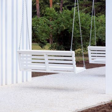White porch swings hanging outdoors with greenery in the background.