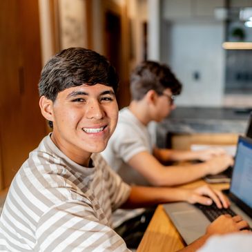 Teenager smiling at camera while working on a laptop indoors.