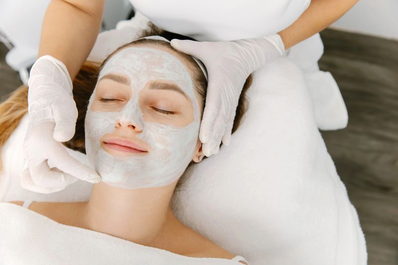 Woman receiving facial skincare treatment with natural ingredients mask applied by professional.