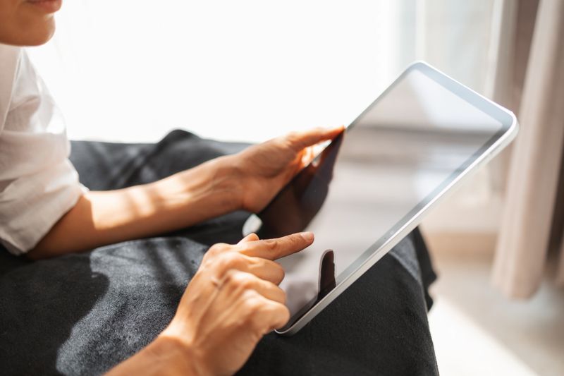 Close-up image of hands interacting with a digital tablet indoors. The scene features soft natural light, creating a calm and modern atmosphere, representing technology usage and connection in daily life.