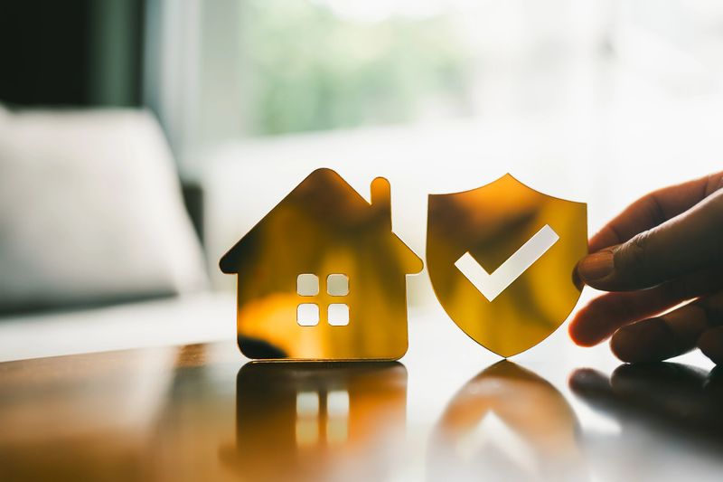 Golden shield with checkmark and house icon symbolizing home insurance, property protection, or real estate security, representing safety, trust, and risk management in housing.