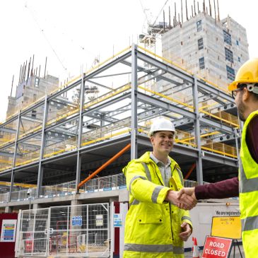 Two construction workers shaking hands at a building site.