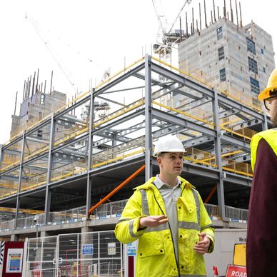 Construction workers discuss progress at a building site with steel framework.