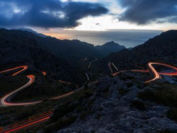 Winding mountain road at dusk with light trails.