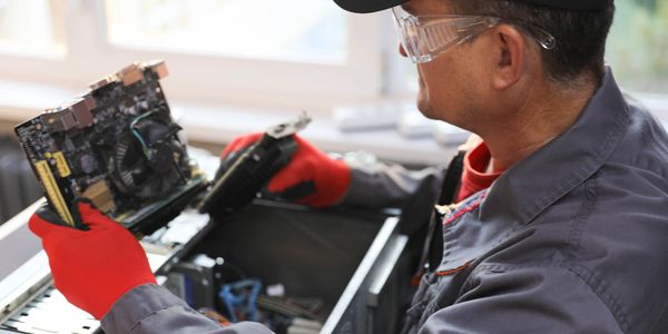 Technician repairing a computer with protective gloves and glasses.