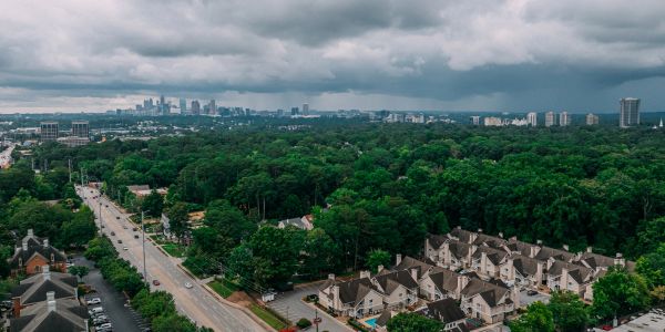 A cloudy city skyline with dense green trees and residential houses.