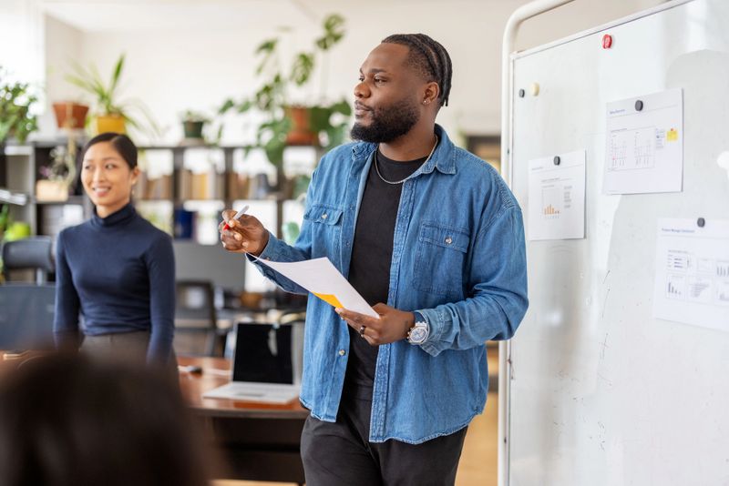 Young African businessman leading a presentation in a modern office, explaining project details to colleagues. Startup entrepreneur leading presentation in modern office.