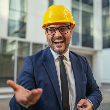 Smiling engineer in a suit and yellow hard hat reaching out.