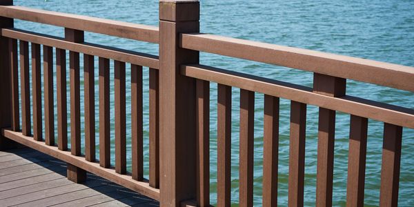 Wooden railing along a waterfront pier with calm blue water.