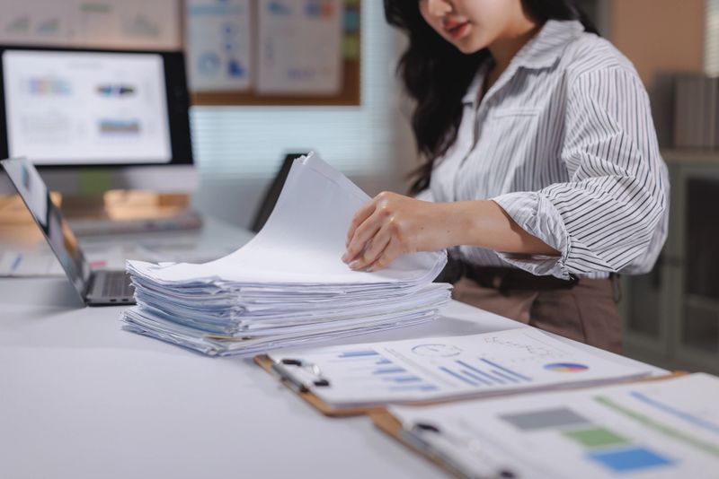 Businesswoman organizing a large stack of documents and reports, working on financial analysis and paperwork at an office desk