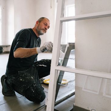 Man painting a white wooden door frame indoors.