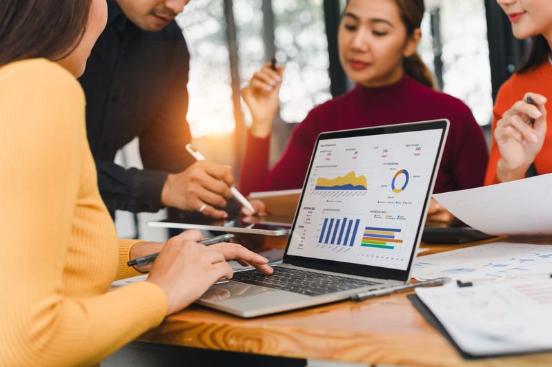 A business team working on data analysis project with laptop showing charts and graphs, discussing strategy in modern office, teamwork and collaboration concept