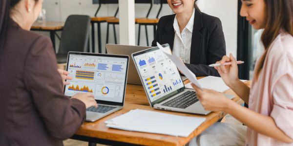 Three women analyzing data on laptops and documents.