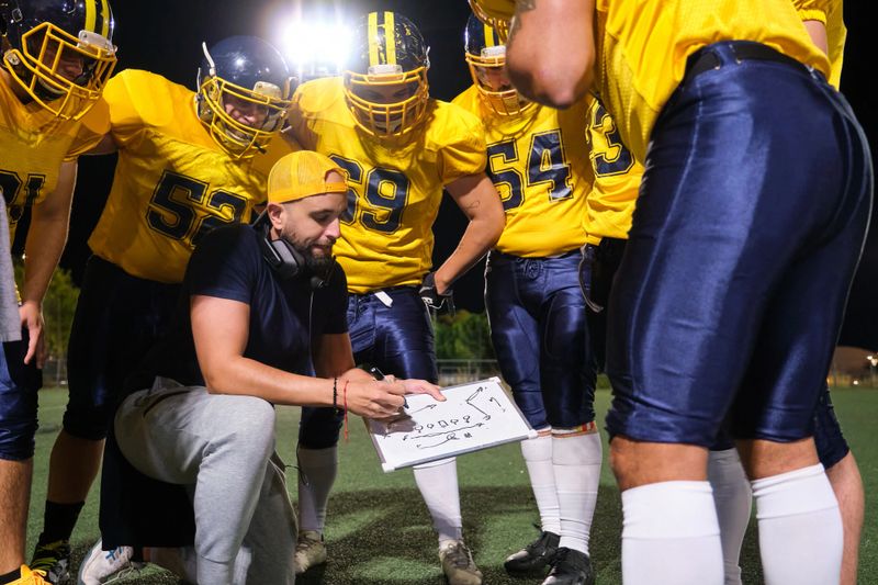 Coach explaining plays to football players in uniform on the field at night