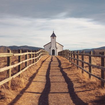 A small white church at the end of a fenced dirt path.