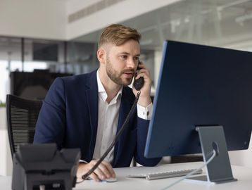 Man in business attire talking on phone at desk with computer.