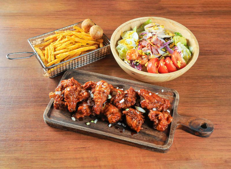 Spicy Glazed Chicken Wings Platter with Seasoned Fries and a Loaded Garden Salad on wooden board side view of main course