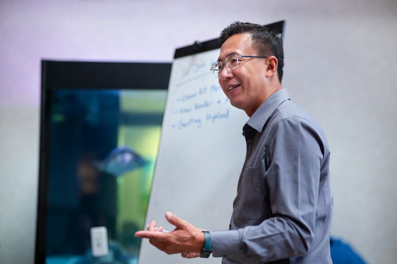 A male office colleague engages the team in dynamic interaction, utilizing the whiteboard to visualize ideas in an open office space.